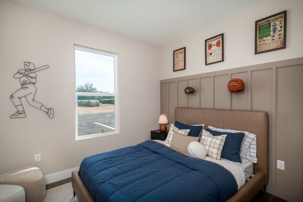 Sports-themed secondary bedroom in the Palomino model with wall molding, athletic décor, and a double bed.