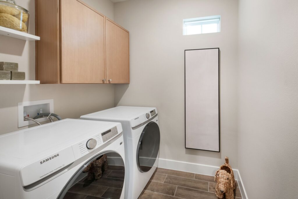 Laundry room in the Palomino model featuring Samsung washer and dryer, upper cabinets, and built-in shelving.